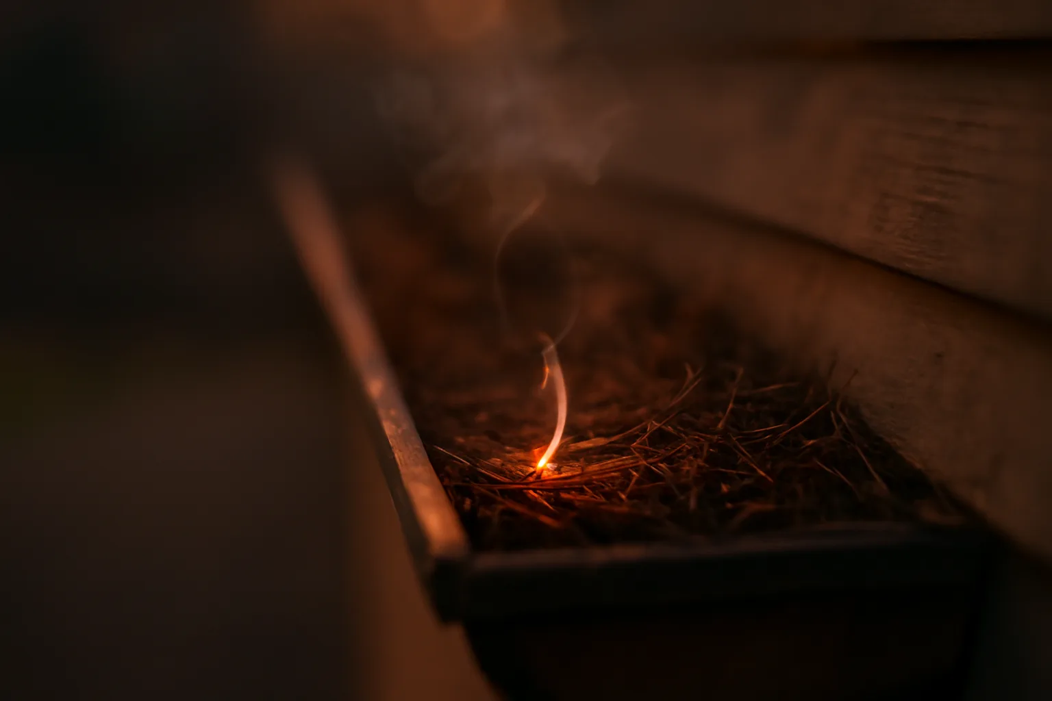 Glowing wind-blown ember landing in a dry gutter on a home's roofline at dusk