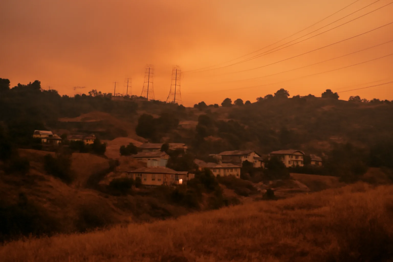 Hillside homes with cleared defensible space beneath power lines at dusk